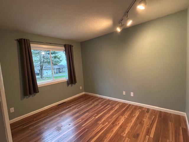 spare room with a textured ceiling, dark hardwood / wood-style flooring, and track lighting