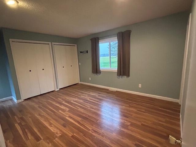 unfurnished bedroom featuring multiple closets, a textured ceiling, and dark hardwood / wood-style flooring