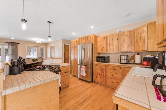 kitchen with sink, light hardwood / wood-style flooring, tile countertops, decorative light fixtures, and appliances with stainless steel finishes