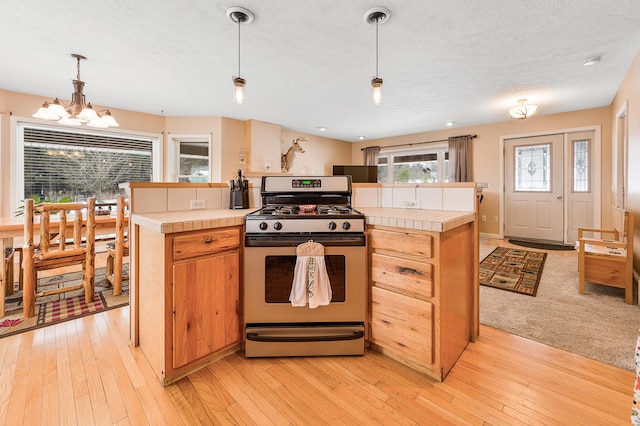 kitchen with gas range oven, an inviting chandelier, light hardwood / wood-style flooring, and tile counters