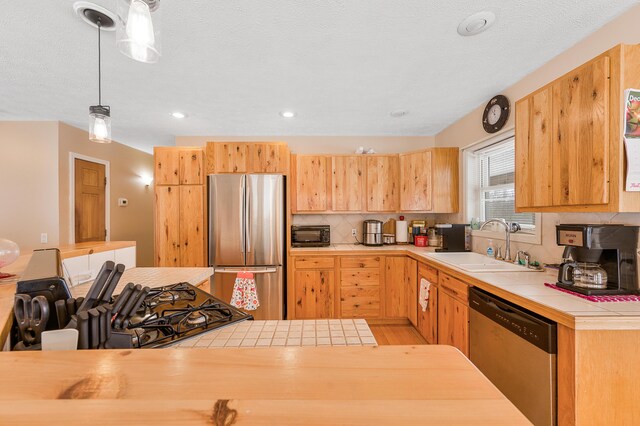 kitchen featuring tile counters, sink, tasteful backsplash, pendant lighting, and appliances with stainless steel finishes