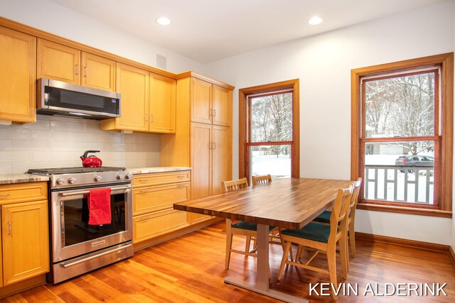 kitchen featuring decorative backsplash, light hardwood / wood-style floors, light stone countertops, and stainless steel appliances