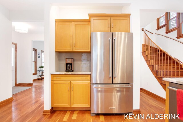 kitchen featuring light stone countertops, backsplash, appliances with stainless steel finishes, and light hardwood / wood-style flooring