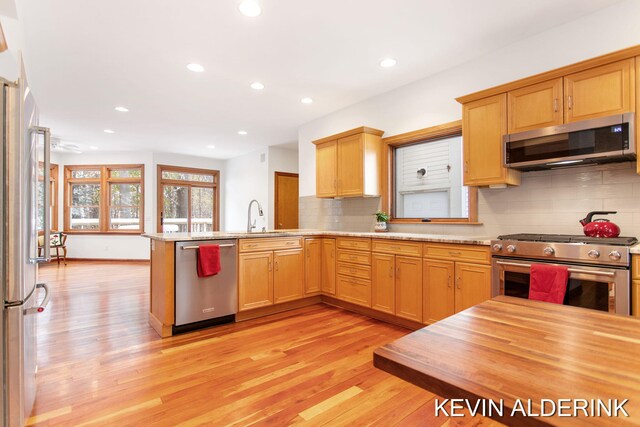 kitchen featuring kitchen peninsula, light wood-type flooring, backsplash, stainless steel appliances, and sink