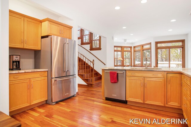 kitchen featuring decorative backsplash, light stone countertops, light hardwood / wood-style flooring, and stainless steel appliances