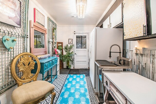 kitchen featuring white refrigerator, white cabinetry, crown molding, and an inviting chandelier