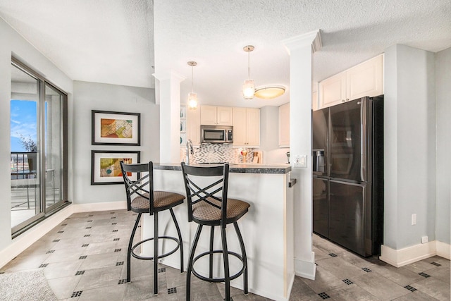 kitchen with backsplash, a textured ceiling, fridge with ice dispenser, white cabinets, and hanging light fixtures