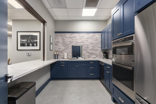 kitchen with light stone countertops, appliances with stainless steel finishes, a paneled ceiling, decorative backsplash, and sink