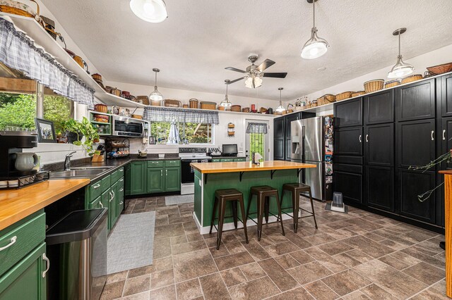 kitchen featuring wooden counters, stainless steel appliances, decorative light fixtures, and sink