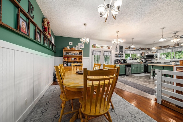 dining area featuring french doors, dark wood-type flooring, wood walls, a textured ceiling, and ceiling fan with notable chandelier