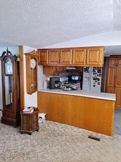 kitchen featuring lofted ceiling, stove, white fridge with ice dispenser, and kitchen peninsula