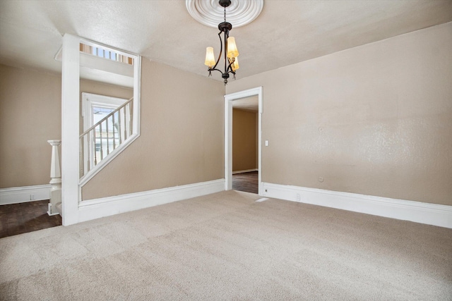 spare room featuring carpet flooring, a textured ceiling, and a notable chandelier