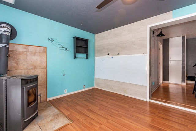 unfurnished living room featuring hardwood / wood-style flooring, a wood stove, and ceiling fan