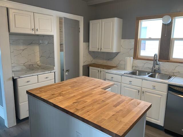 kitchen with a center island, sink, stainless steel dishwasher, butcher block countertops, and white cabinetry