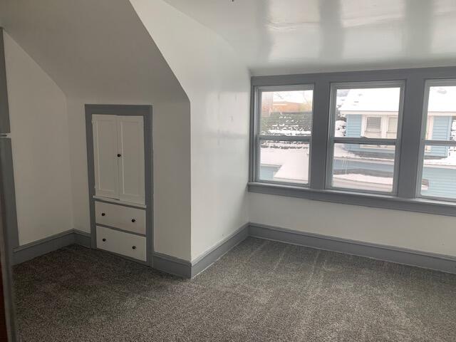 bonus room with dark colored carpet and lofted ceiling