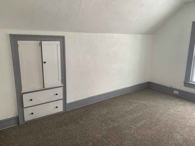 bonus room featuring a textured ceiling, dark carpet, and lofted ceiling