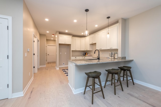 kitchen with white cabinetry, sink, decorative light fixtures, and light wood-type flooring