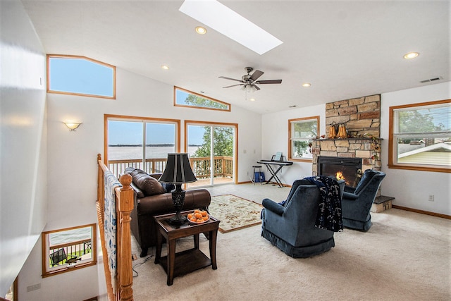 living room featuring light carpet, a skylight, ceiling fan, a water view, and a stone fireplace