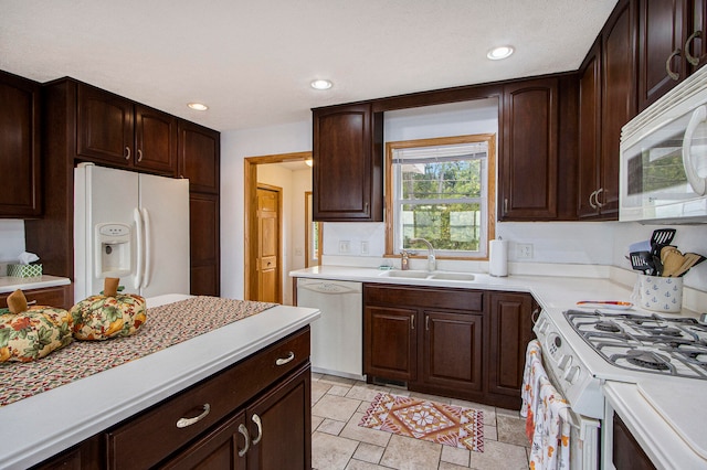 kitchen with dark brown cabinetry, white appliances, and sink