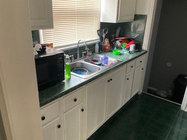 kitchen with dark tile patterned floors, white cabinetry, and sink