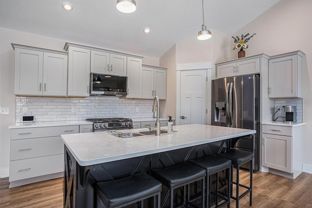 kitchen with gray cabinets, appliances with stainless steel finishes, sink, decorative backsplash, and a kitchen island with sink