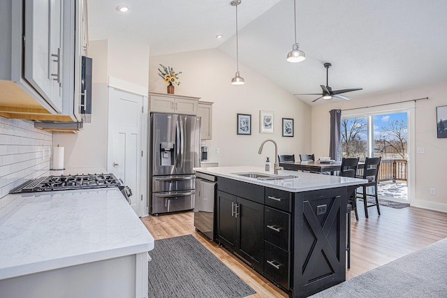 kitchen with sink, stainless steel fridge, dishwasher, a kitchen island with sink, and decorative light fixtures