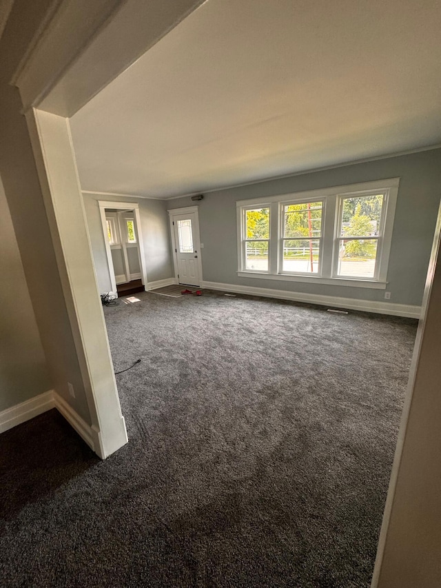 unfurnished living room with a wealth of natural light and dark colored carpet