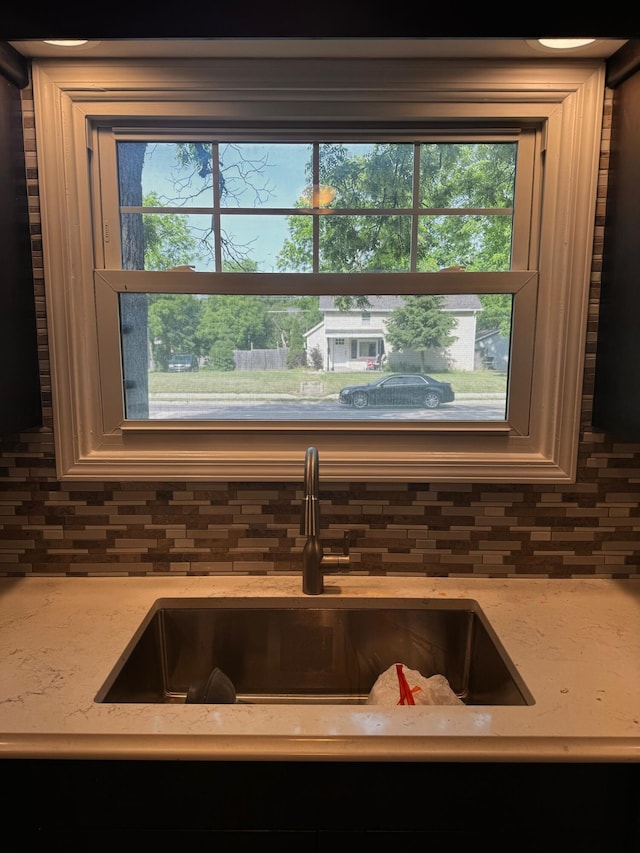 interior details featuring backsplash, light stone countertops, and sink