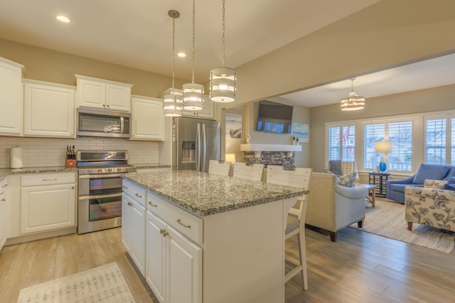 kitchen with light stone countertops, appliances with stainless steel finishes, pendant lighting, a center island, and white cabinetry