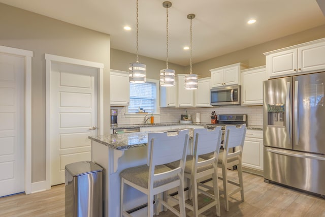 kitchen featuring hanging light fixtures, a kitchen island, stone countertops, white cabinets, and appliances with stainless steel finishes