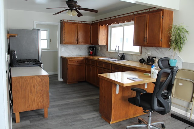 kitchen with wood-type flooring, stainless steel refrigerator, kitchen peninsula, decorative backsplash, and sink