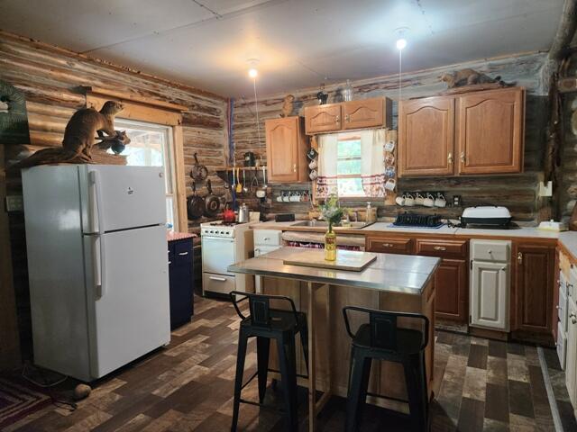 kitchen featuring a kitchen bar, rustic walls, white appliances, a center island, and dark hardwood / wood-style floors