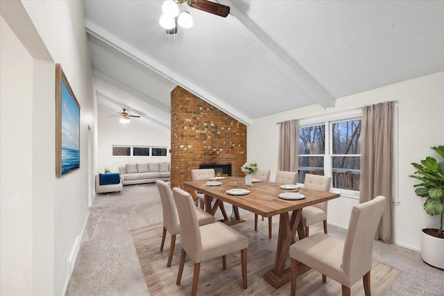 dining room featuring lofted ceiling with beams, ceiling fan, light carpet, and a brick fireplace