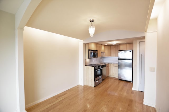 kitchen featuring light hardwood / wood-style floors, appliances with stainless steel finishes, decorative light fixtures, vaulted ceiling, and sink