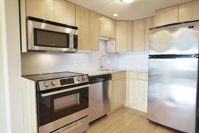 kitchen featuring light hardwood / wood-style floors, appliances with stainless steel finishes, light brown cabinets, light stone counters, and sink