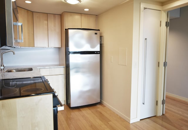 kitchen featuring stainless steel fridge, light brown cabinetry, light hardwood / wood-style flooring, light stone counters, and sink