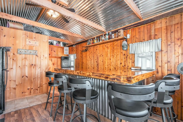 kitchen with black refrigerator, hardwood / wood-style flooring, beamed ceiling, and wood walls