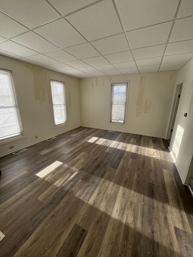 empty room with a drop ceiling, a healthy amount of sunlight, and dark wood-type flooring