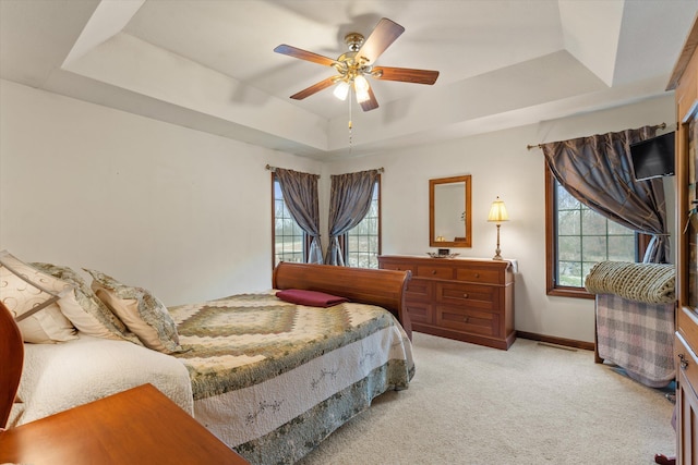 bedroom with ceiling fan, light carpet, and a tray ceiling