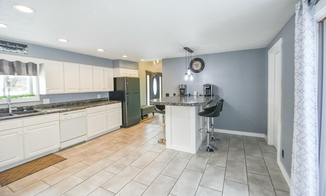 kitchen featuring white cabinetry, dishwasher, black refrigerator, pendant lighting, and a breakfast bar