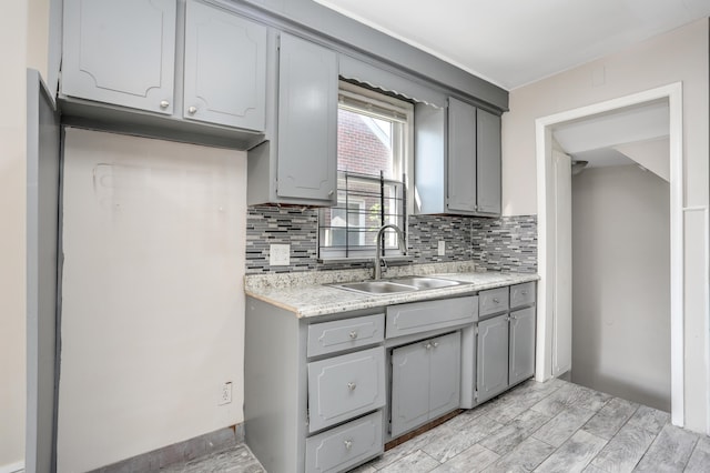 kitchen with backsplash, gray cabinetry, sink, and light hardwood / wood-style flooring