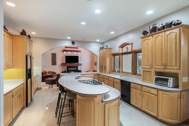 kitchen featuring dishwasher, sink, kitchen peninsula, light brown cabinetry, and a breakfast bar