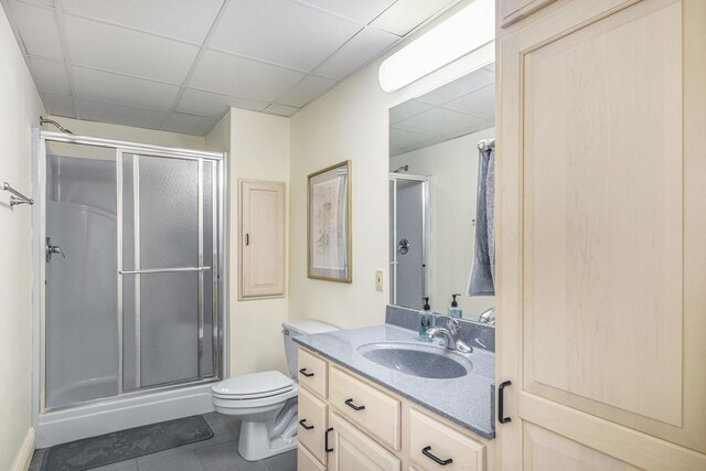 bathroom with a paneled ceiling, vanity, tile patterned flooring, toilet, and a shower with shower door