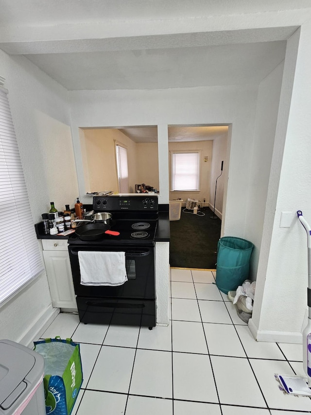 kitchen featuring black electric range, light tile patterned floors, and white cabinets