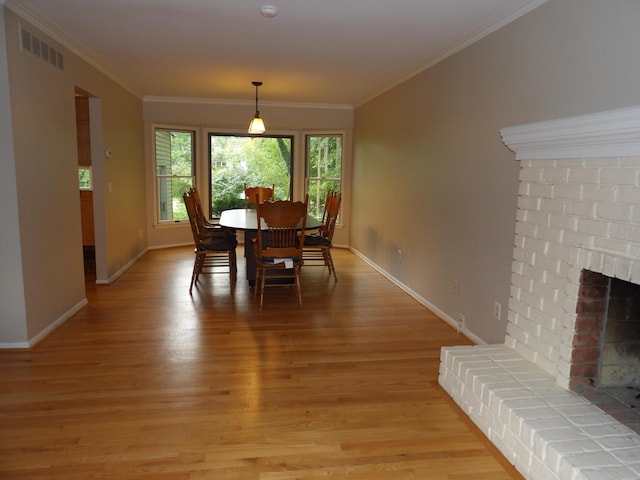 dining area with ornamental molding, light wood-type flooring, and a brick fireplace