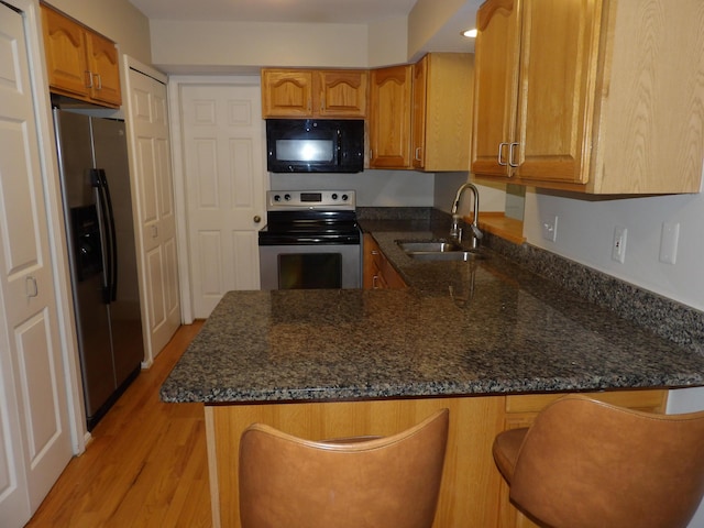 kitchen with light wood-type flooring, kitchen peninsula, dark stone countertops, and appliances with stainless steel finishes