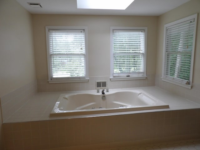 bathroom featuring a skylight, tile patterned floors, and tiled tub