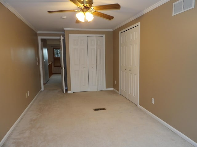 unfurnished bedroom featuring two closets, light colored carpet, ceiling fan, and crown molding