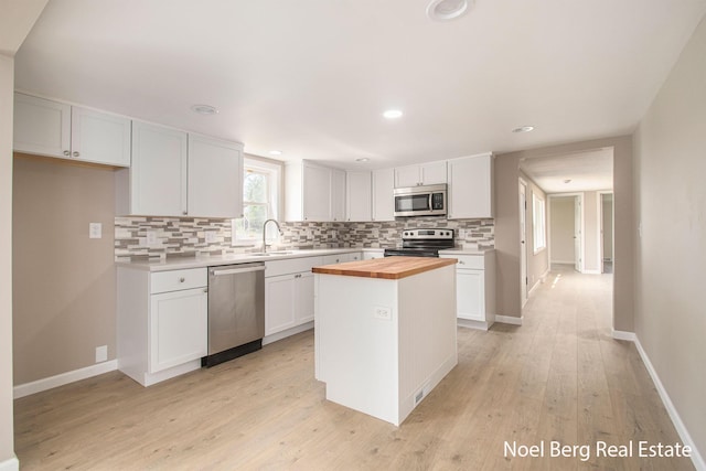 kitchen with stainless steel appliances, wooden counters, a kitchen island, and white cabinets