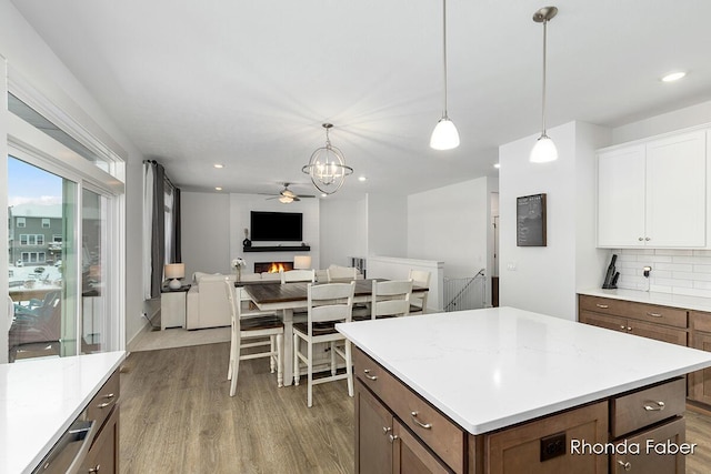 kitchen featuring decorative backsplash, light wood-type flooring, ceiling fan with notable chandelier, pendant lighting, and white cabinets